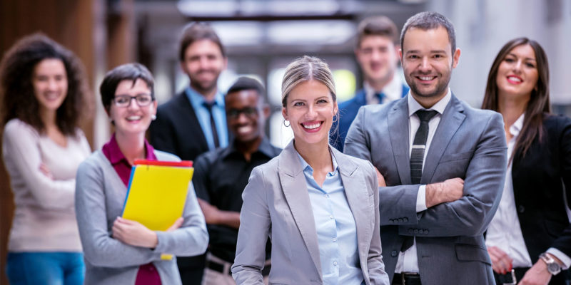 diverse group of professional men and women standing in office and smiling because services credits make it easier to buy and sell professional services and improves customer experience.