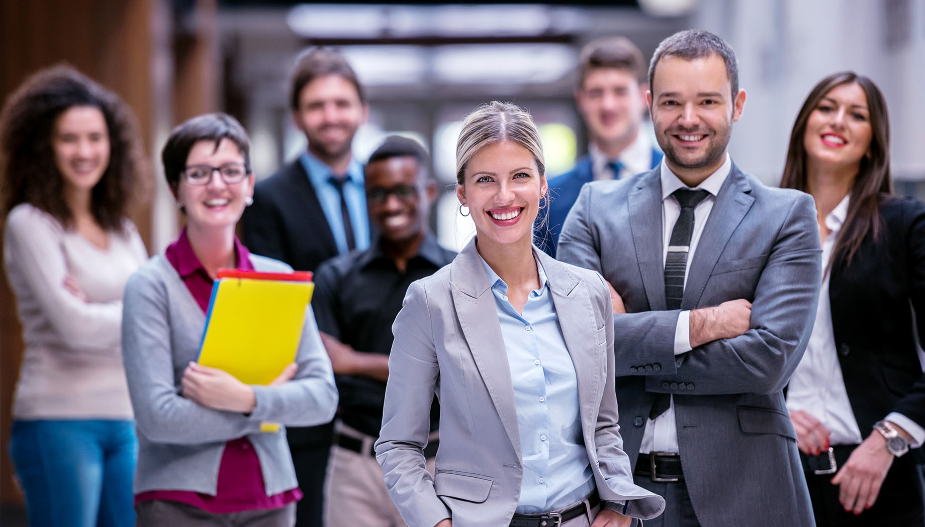 diverse group of professional men and women standing in office and smiling because services credits make it easier to buy and sell professional services and improves customer experience.